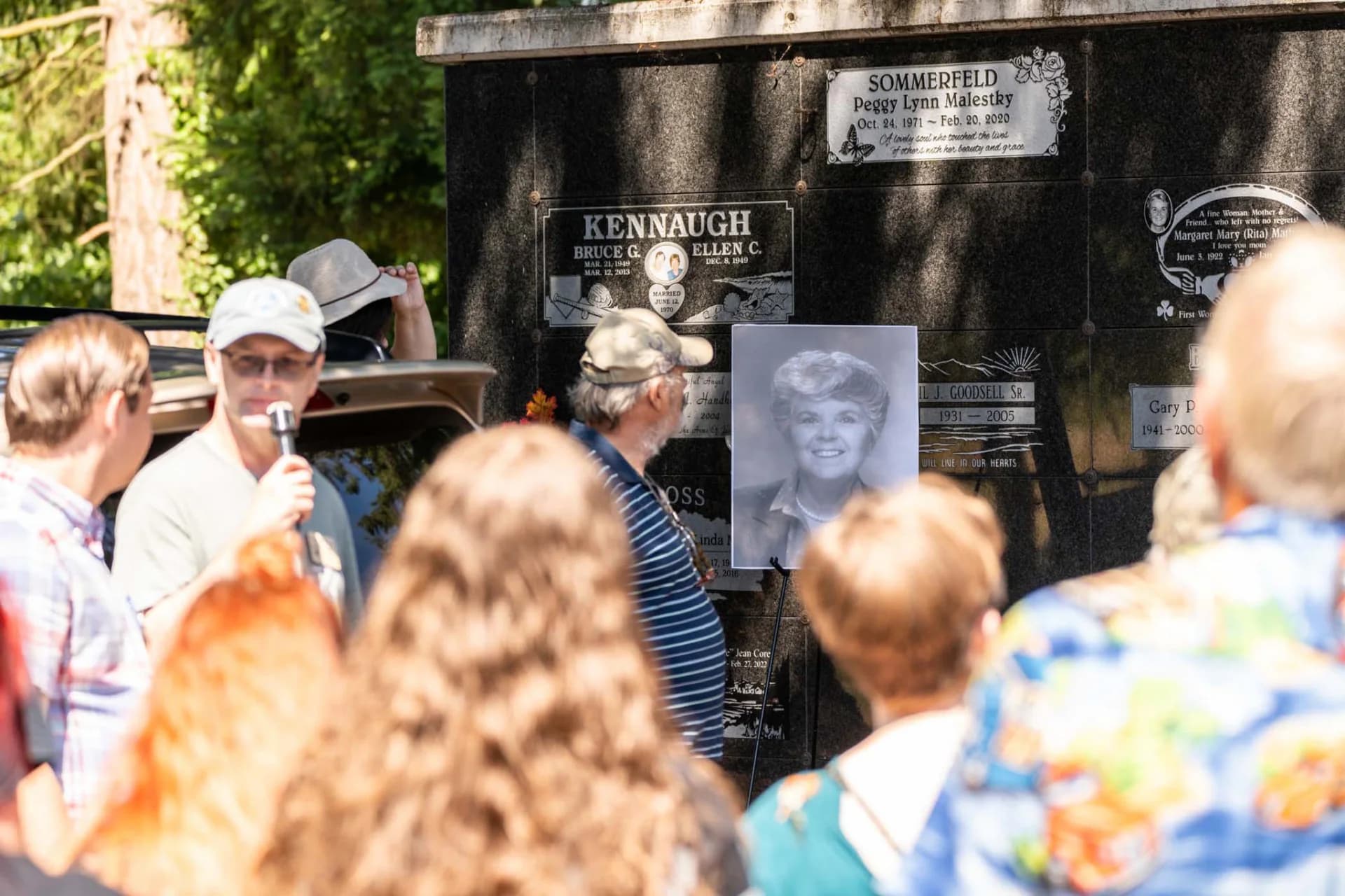Visitors listen to a life story beside memorial plaques and a portrait during the 2025 tour