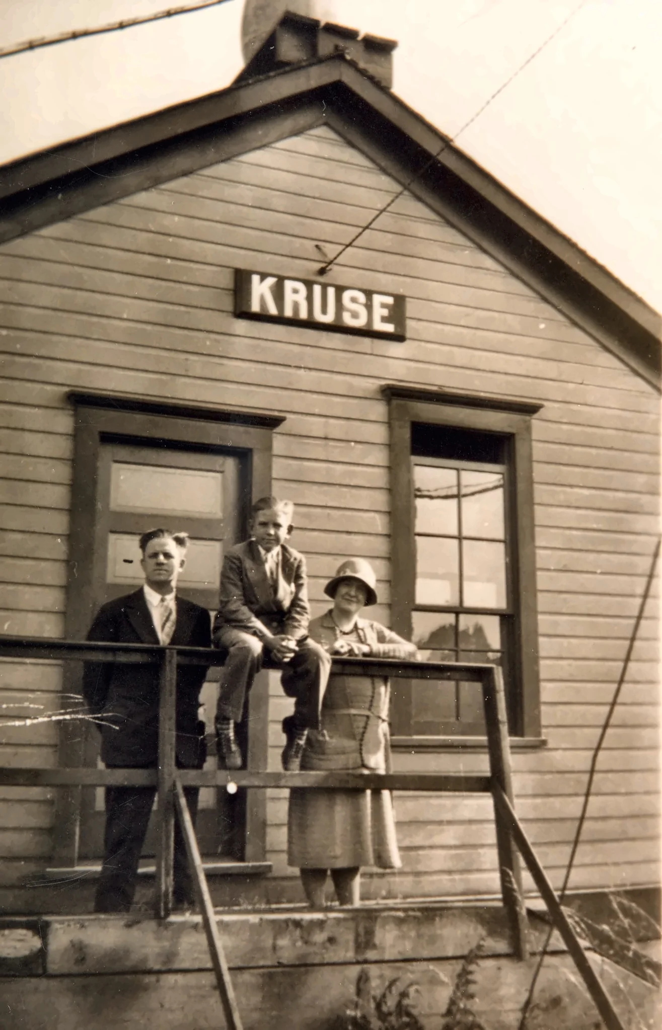 Three people posed on the steps of a wooden building marked Kruse