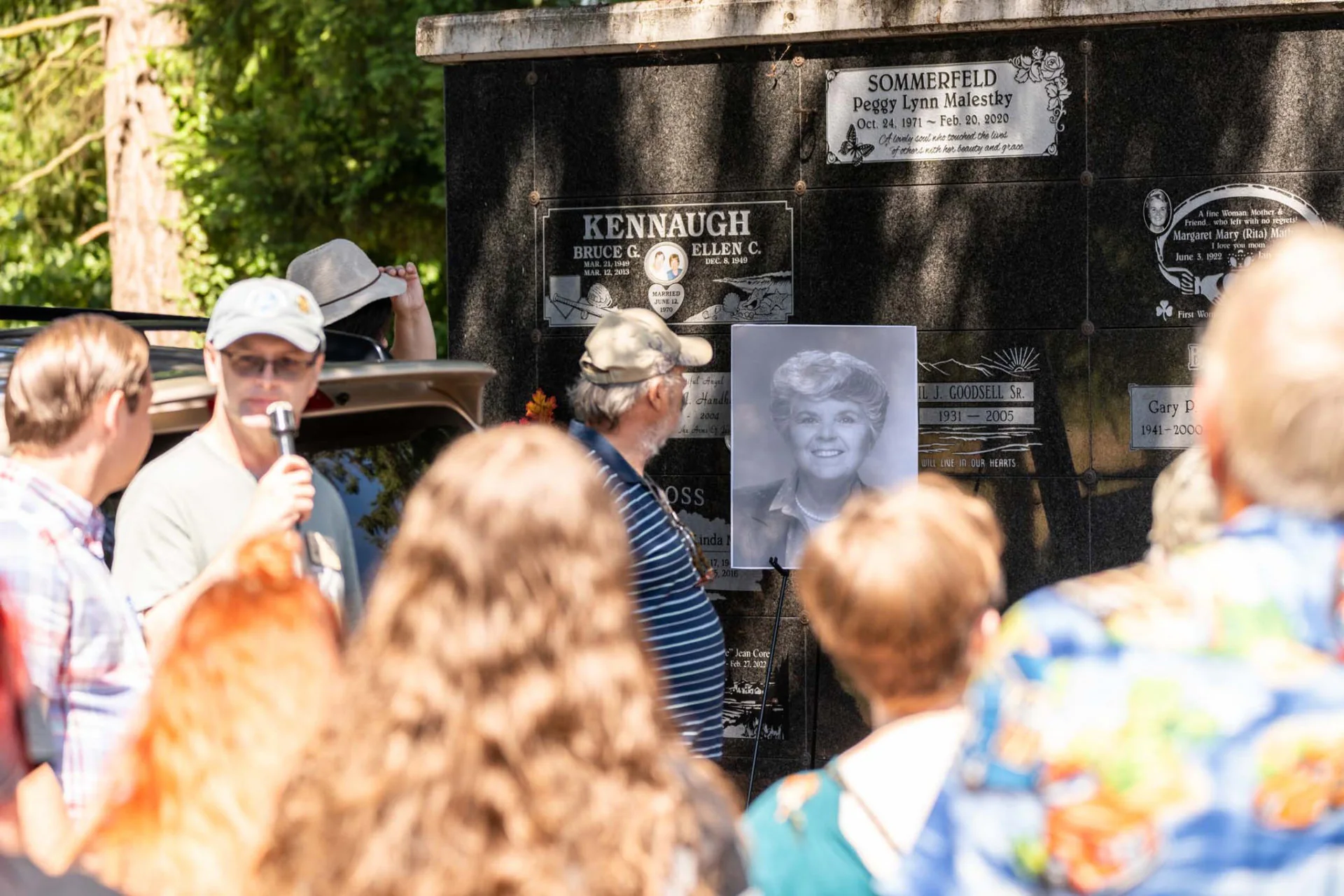 Visitors listen to a life story beside memorial plaques and a portrait during the 2025 tour